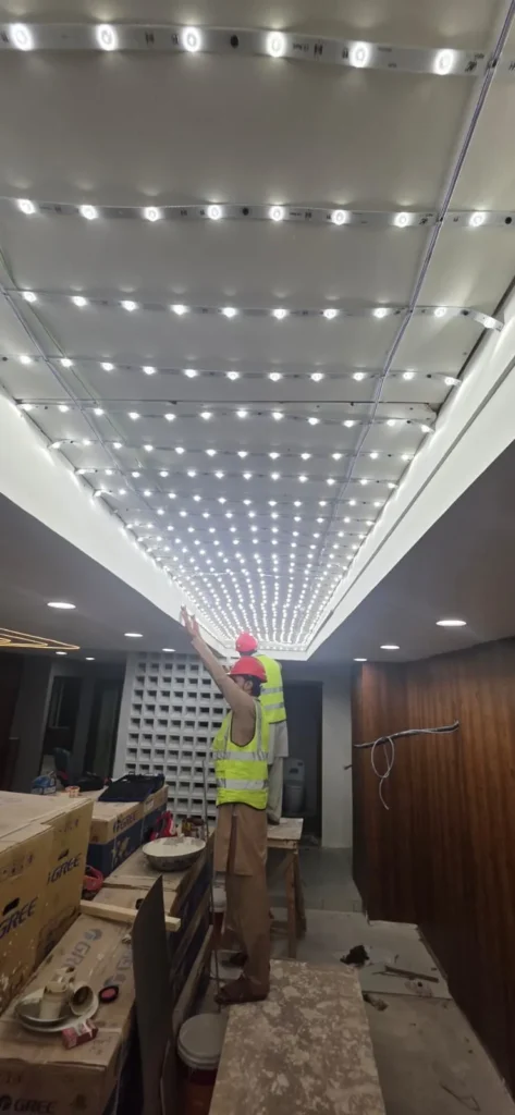Led modules for White plain backlit stretch fabric ceiling panel installed within a wooden coffer grid at a corporate office entrance in Islamabad